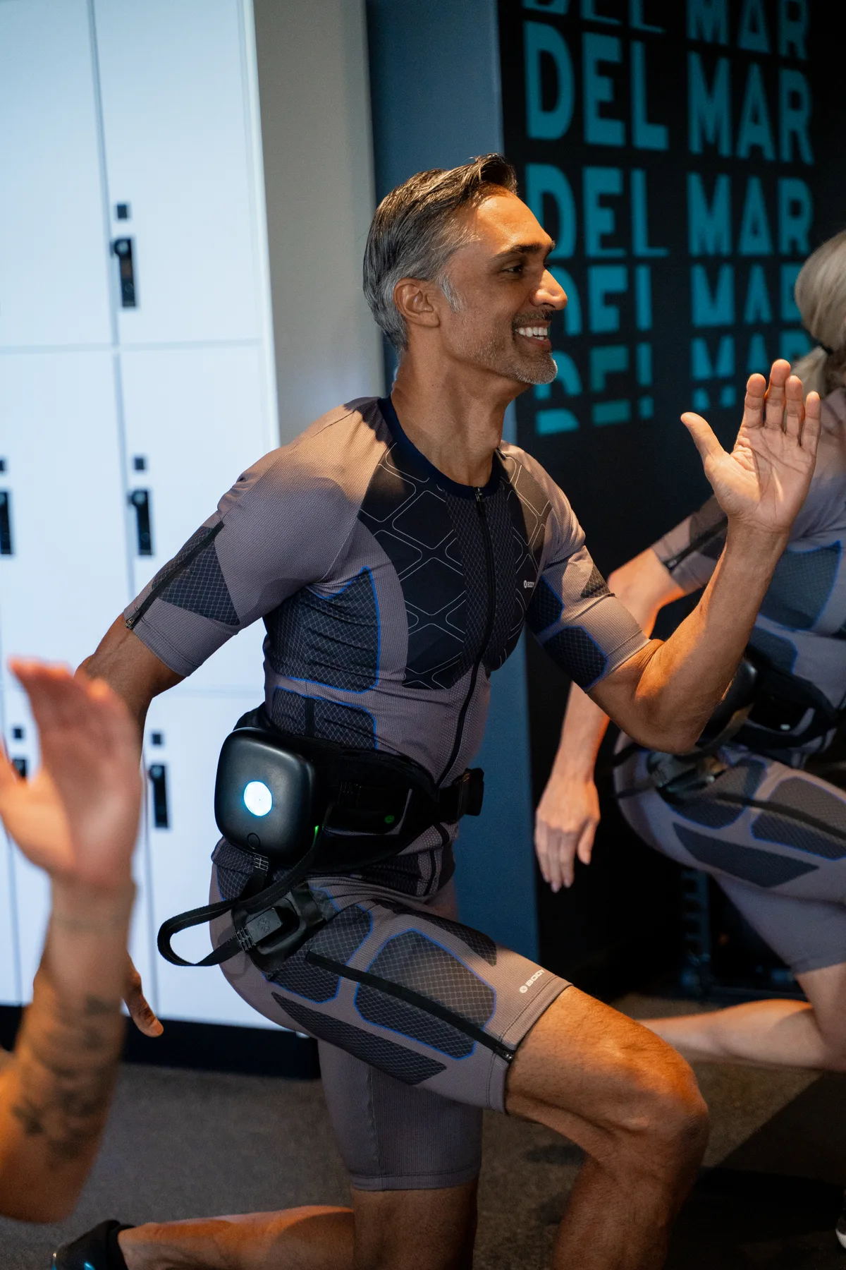 Member in EMS suit high-fiving her coach after a session at BODY20 North Scottsdale, genuine smile, studio lockers visible in background.